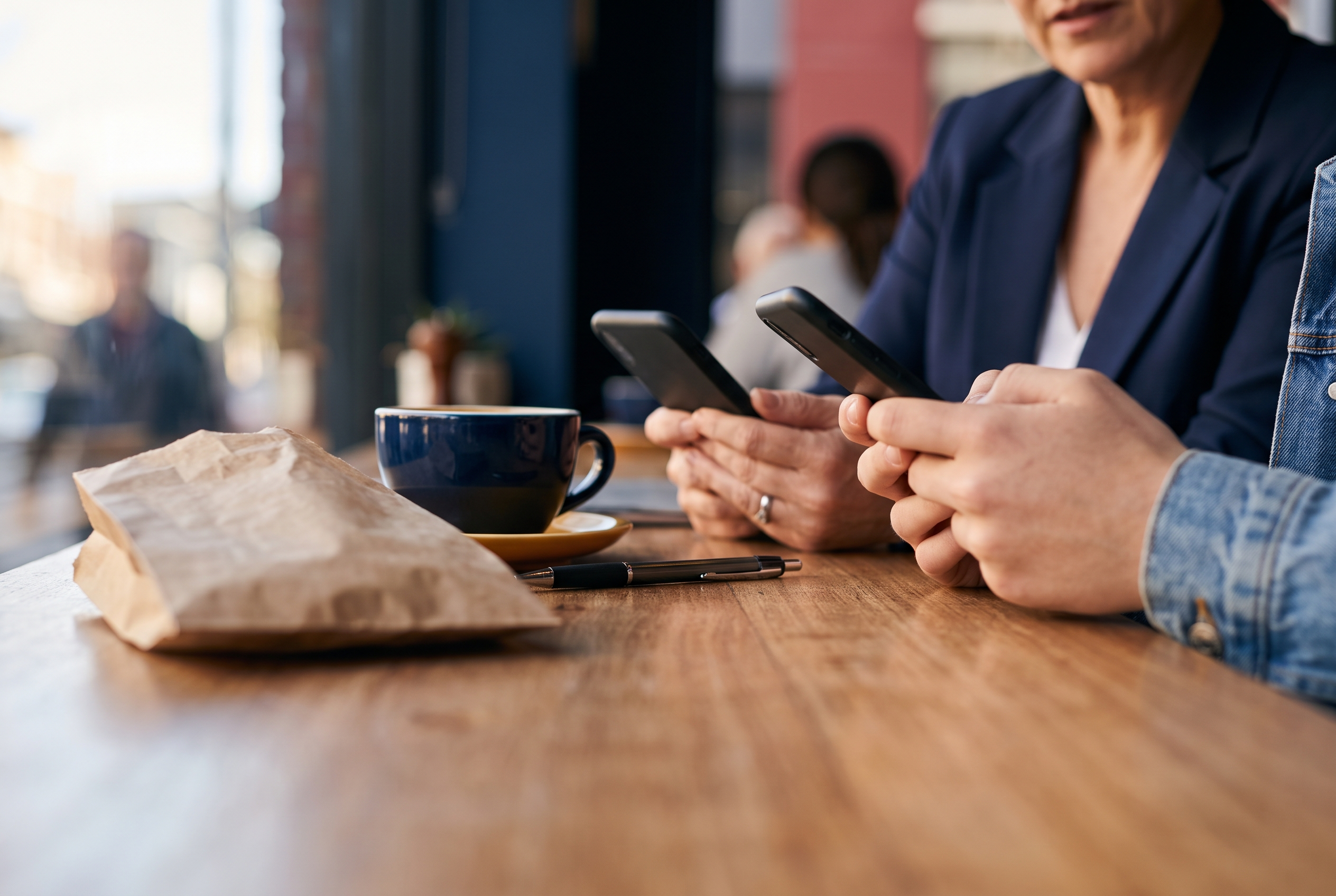 Gen X professional and Gen Z shopper each on their phones at a cafe table, illustrating generational differences in Australian eCommerce trends